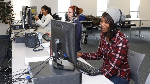 Three women, two of which are wearing headsets, training and working at individual computers, in one of our UFCW rental computer labs.