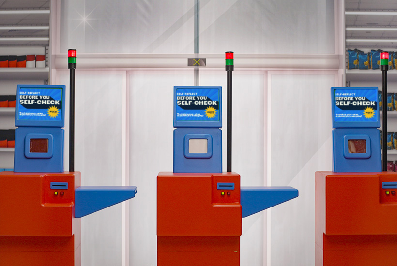 Three blue and red self-checkout machines that are not in use are positioned at the front interior of a grocery store.